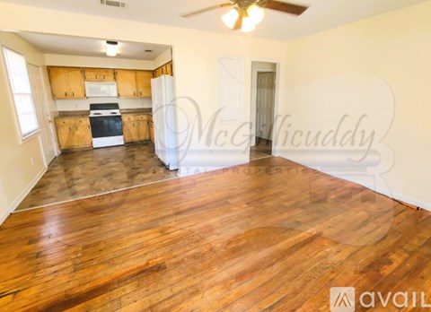 A spacious room with wooden flooring and a kitchen area in the background.