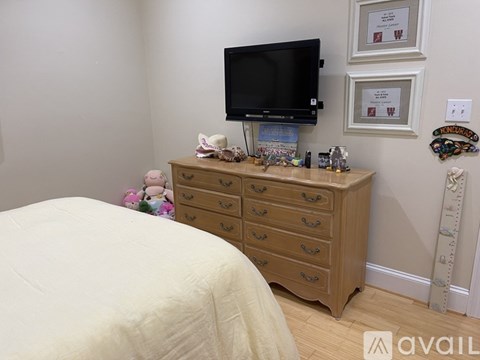 A bedroom with a bed, a dresser with a television on top, and some decorations on the wall.