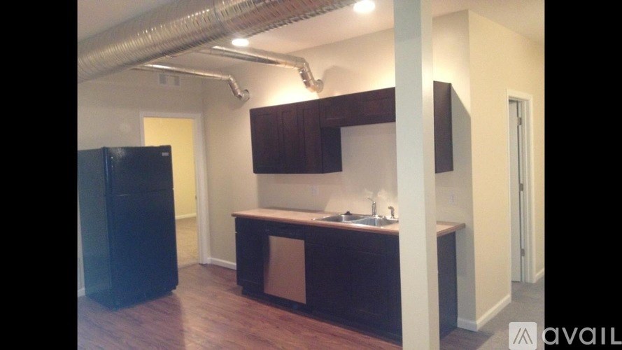A kitchen area with a black refrigerator and wooden cabinets.