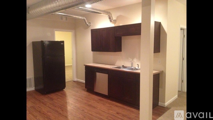A kitchen area with a black fridge and wooden floors.