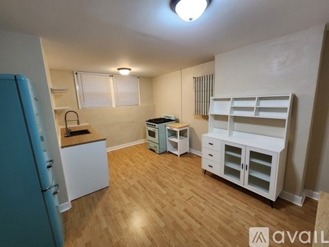 A kitchen area with a blue refrigerator, white cabinets, and a wooden floor.