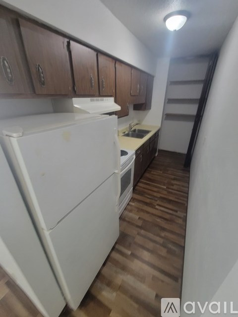 A small kitchen with a white fridge and wooden floors.