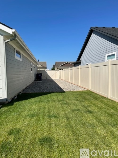 A backyard with a white fence and a gravel path leading to a house.