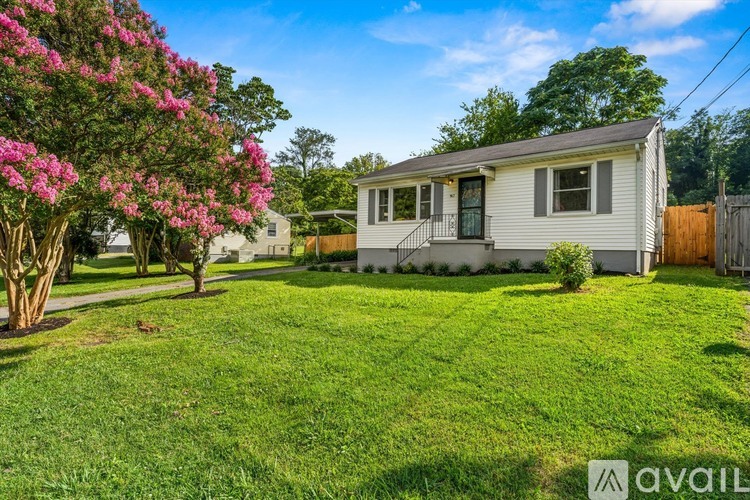 A house with a white exterior is surrounded by a green lawn and a flowering tree.