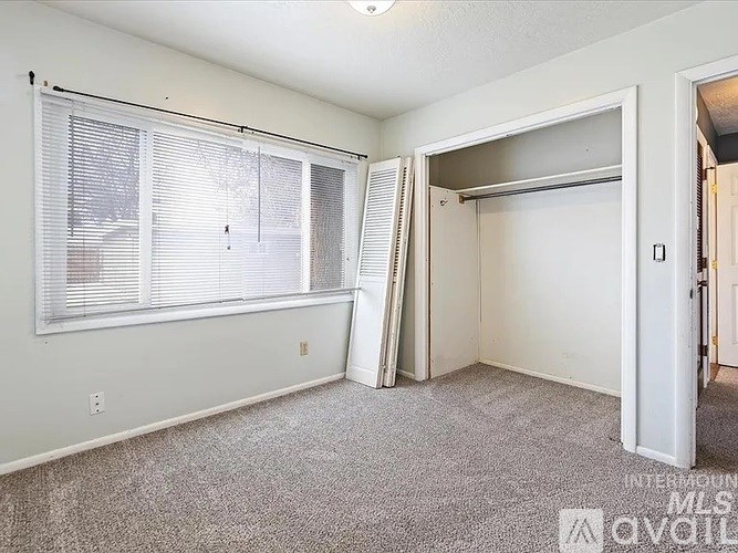 A room with a carpeted floor, a window with blinds, and a sliding door.