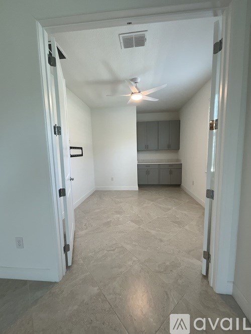 A room with a ceiling fan and a door on the left.