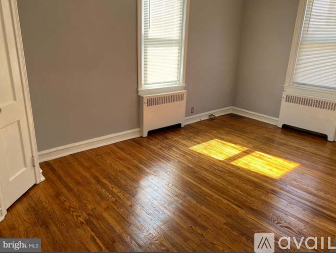 A room with wooden flooring and two windows.