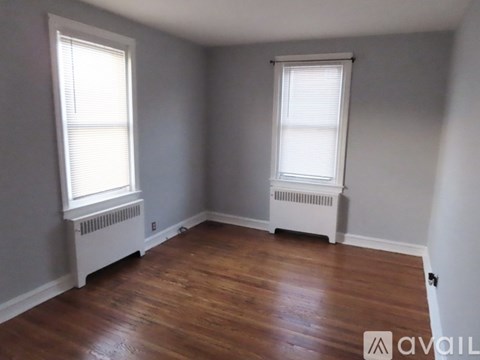 A room with wooden floors and two windows with white blinds.