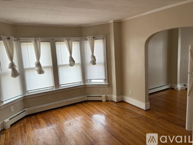 A room with wooden floors and a large window with white curtains.