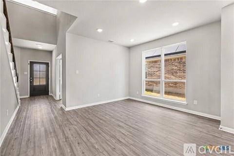 A spacious room with wooden flooring and a large window overlooking a brick wall.