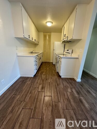 A kitchen with white appliances and wooden floors.