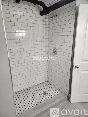 A white tiled shower with a drain in the middle.