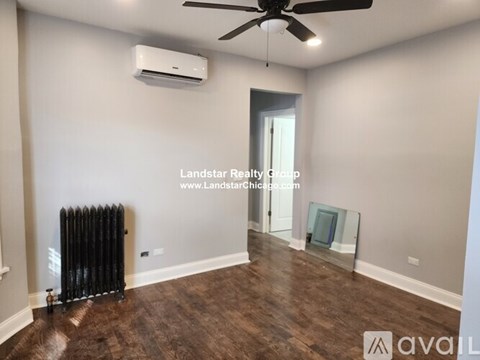 A room with a fan, air conditioner, and wood flooring.