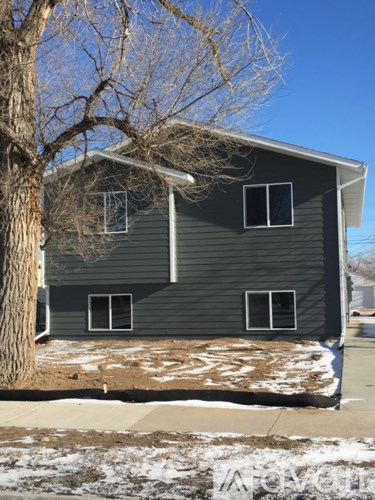 A house with a grey siding and a tree in front of it.