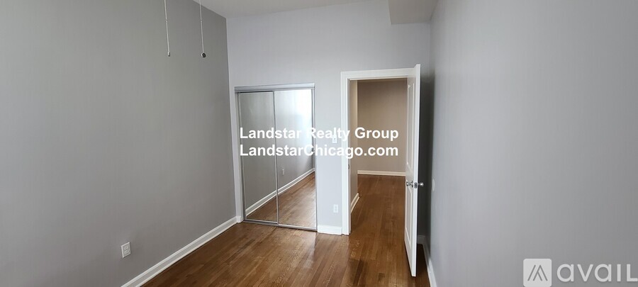 A room with a wooden floor and white walls, with a doorway leading to another room.
