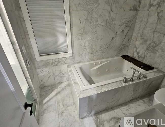 A bathroom with a marble patterned floor and walls, a white sink, and a window with blinds.