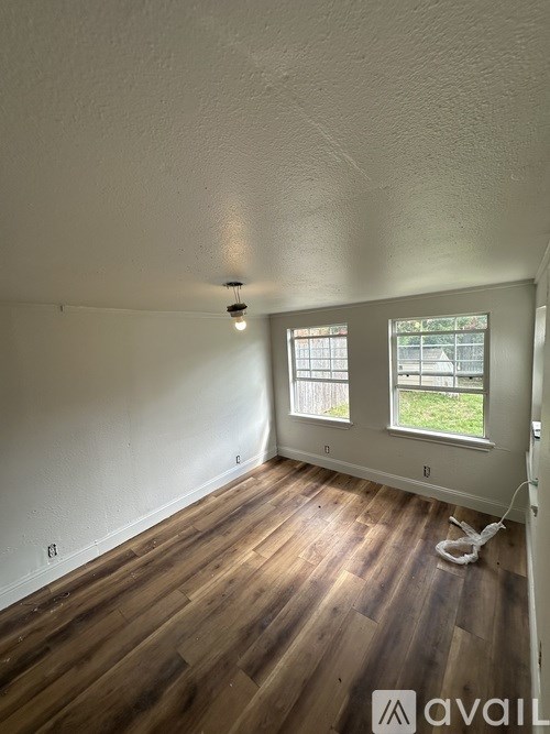 A room with wooden floors and a window showing a fence and greenery outside.