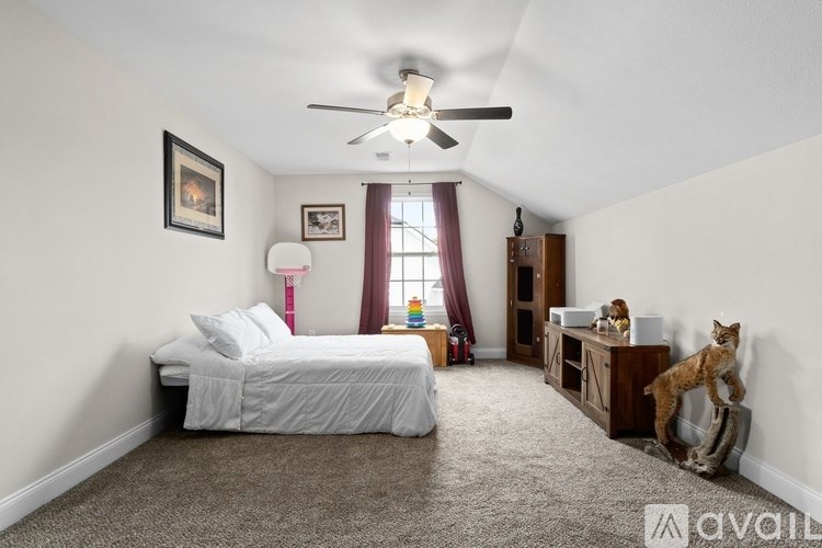 A bedroom with a bed, a fan, a window with curtains, and a picture on the wall.