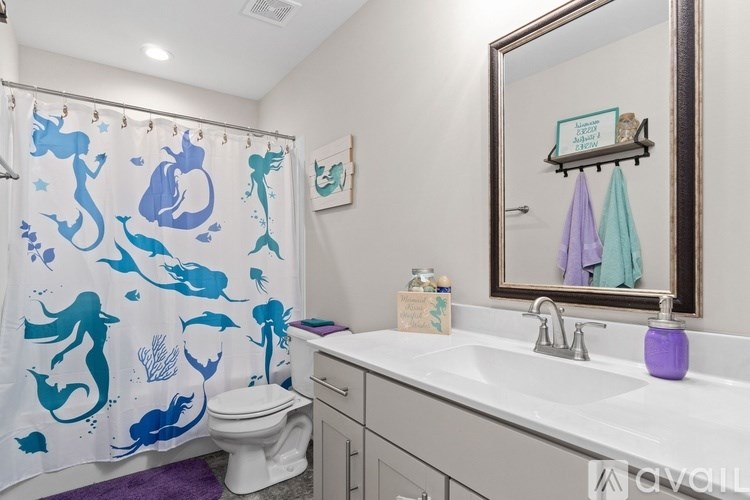 A bathroom with a white toilet and a shower curtain with blue fish on it.