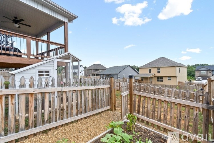 A wooden fence surrounds a backyard with a patio and a house in the background.
