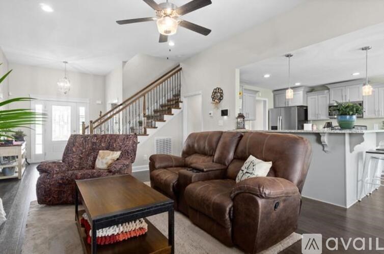 A living room with brown leather furniture and a staircase in the background.