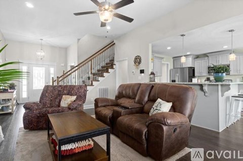 A living room with brown leather furniture and a staircase in the background.