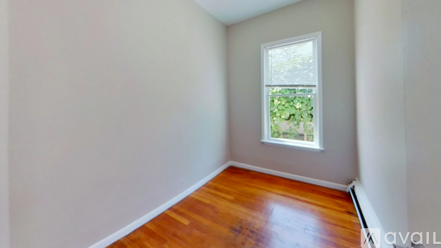 A room with a wooden floor and a window showing greenery outside.