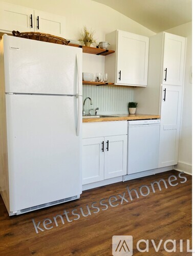 A white refrigerator in a kitchen with wooden floors and white cabinets.