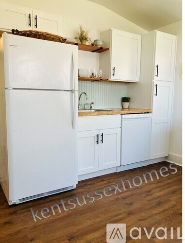 A white refrigerator in a kitchen with wooden floors and white cabinets.