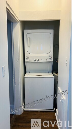 A small white washing machine sits in a narrow space between a wall and a door.