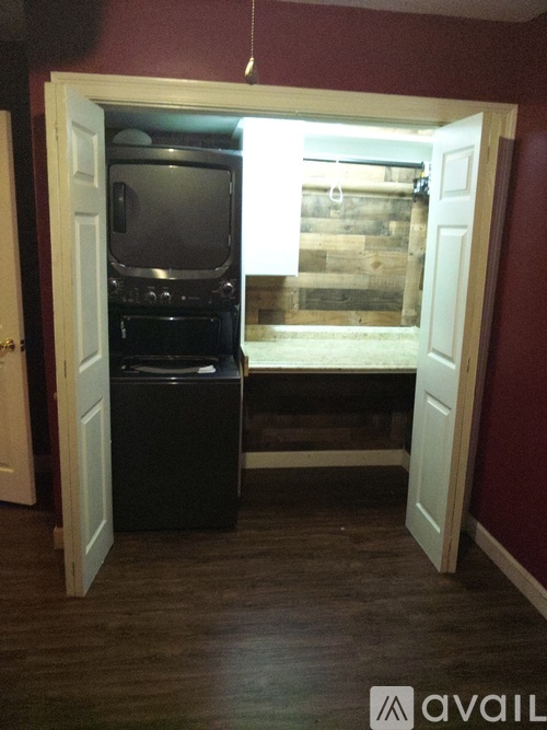 A black refrigerator is in a room with a wooden floor and a doorway leading to a balcony.