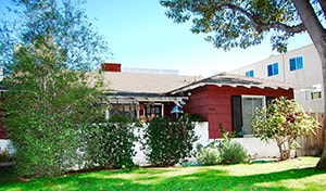 A red house with a white fence and green bushes in front.