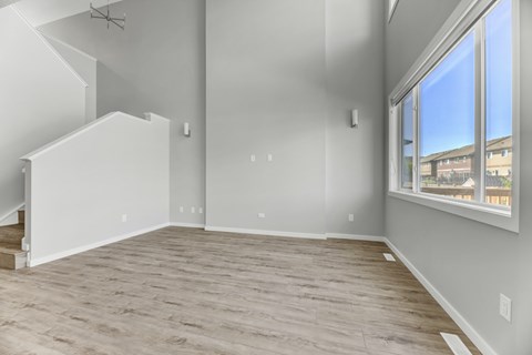 A spacious room with light wood flooring and a staircase on the left side.