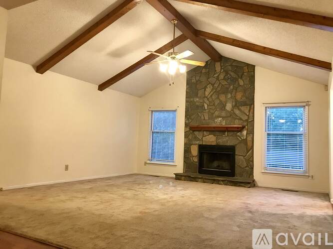 A living room with a stone fireplace and a fan on the ceiling.