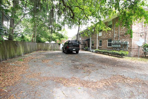 A black car is parked in a driveway with a wooden fence and trees.