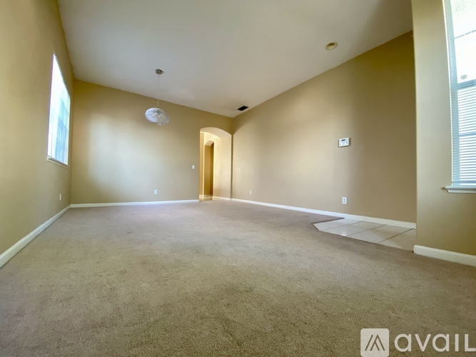 A spacious room with beige carpeting and a doorway leading to another room.