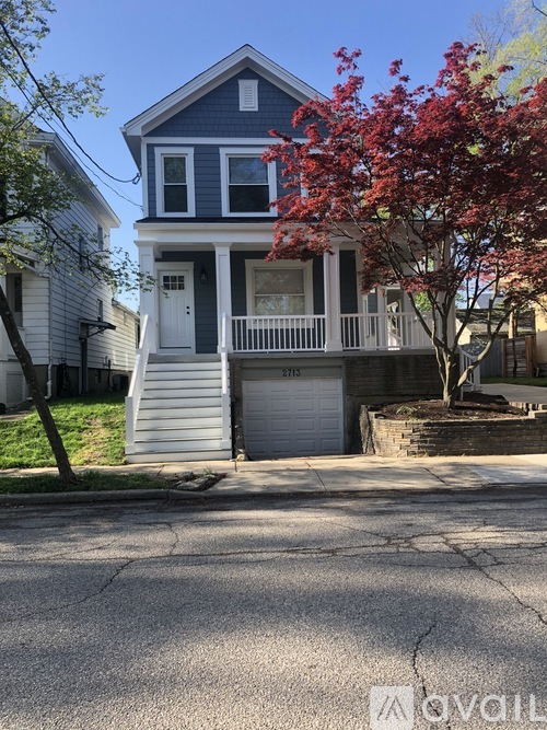 A blue house with a white door and windows is in front of a tree with red leaves.