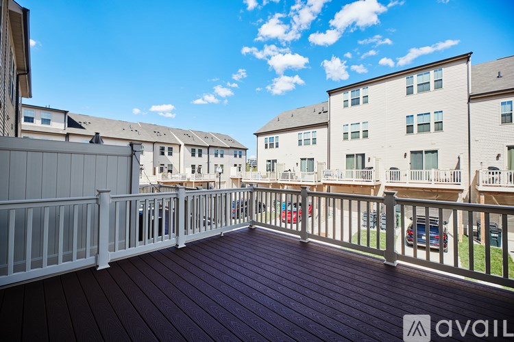 A balcony with a wooden floor and white railings overlooks a row of apartment buildings.