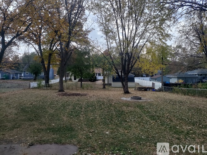A grassy field with trees and a few houses in the background.