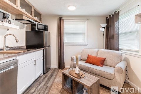 A kitchen with a dishwasher, microwave, and oven is adjacent to a living room with a couch and a coffee table.