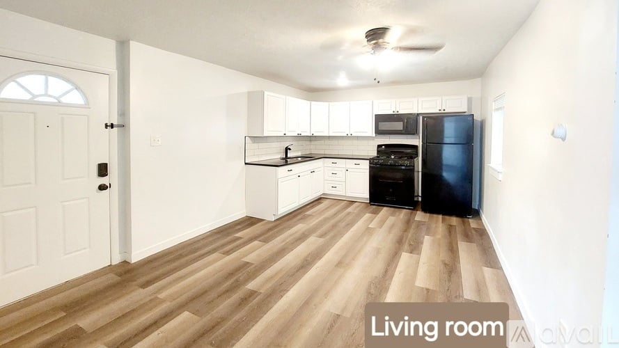 A living room with a wooden floor and a kitchen area in the background.