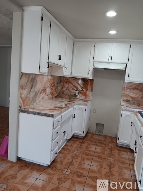 A kitchen with white cabinets and brown tiled floors.