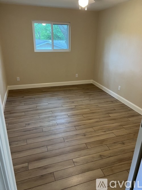 A room with wooden flooring and a window showing a view of trees.