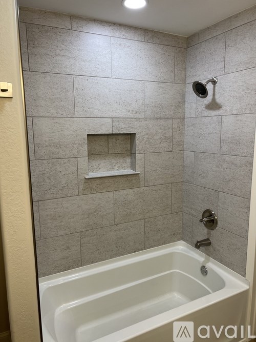 A bathroom with a white tub and grey tiled walls.