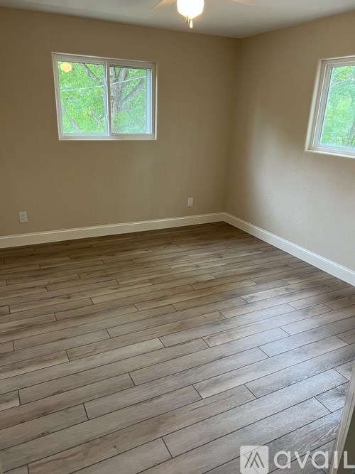A room with wooden flooring and two windows.
