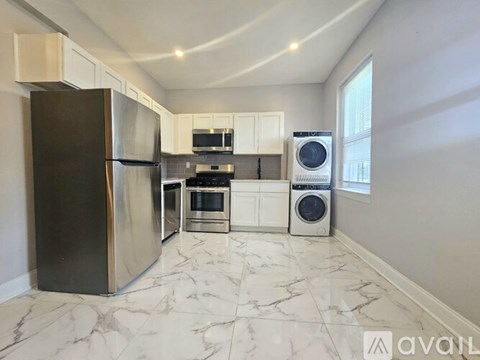 A kitchen with a black fridge, white cabinets, and a marble floor.