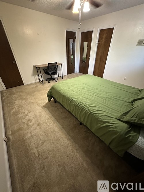 A bedroom with a green bedspread and a desk with a chair.