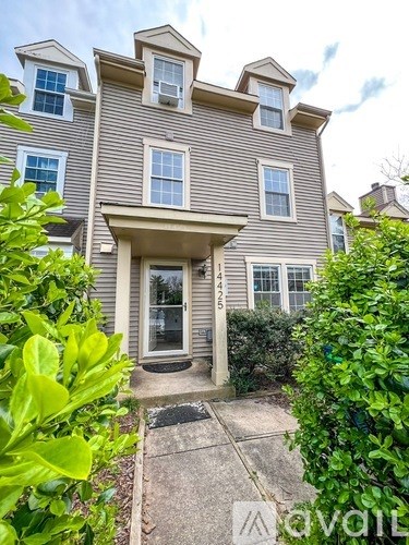 A grey house with a white door and windows surrounded by greenery.