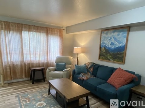 A living room with a blue couch, a chair, a table, and a painting on the wall.