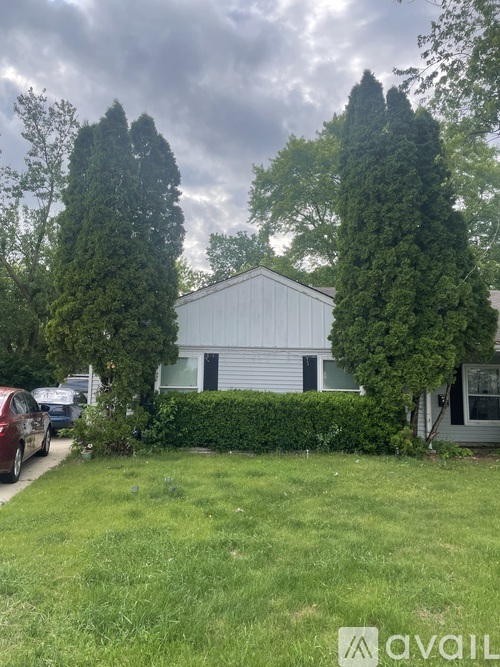 A house with a white garage door is surrounded by greenery and trees.